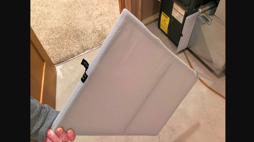 Person holding clean HVAC air filter with white mesh cover, standing near furnace in residential utility room