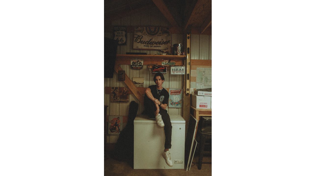 Person sitting on a white chest freezer in a rustic garage with vintage signs and boxes around