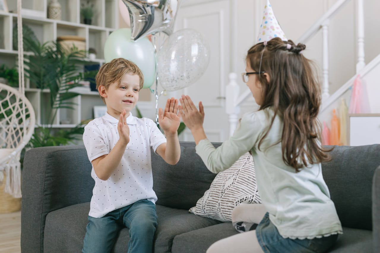 Two children playing a hand-clapping game on a couch during a birthday party