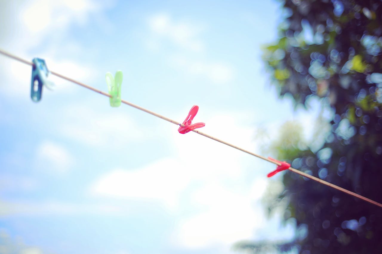 Clothesline with colorful clothespins under a clear blue sky, trees in background