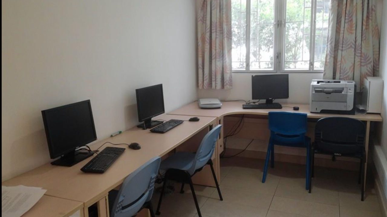 Computer room with desks, monitors, keyboards, chairs, printer, and scanner near a large window