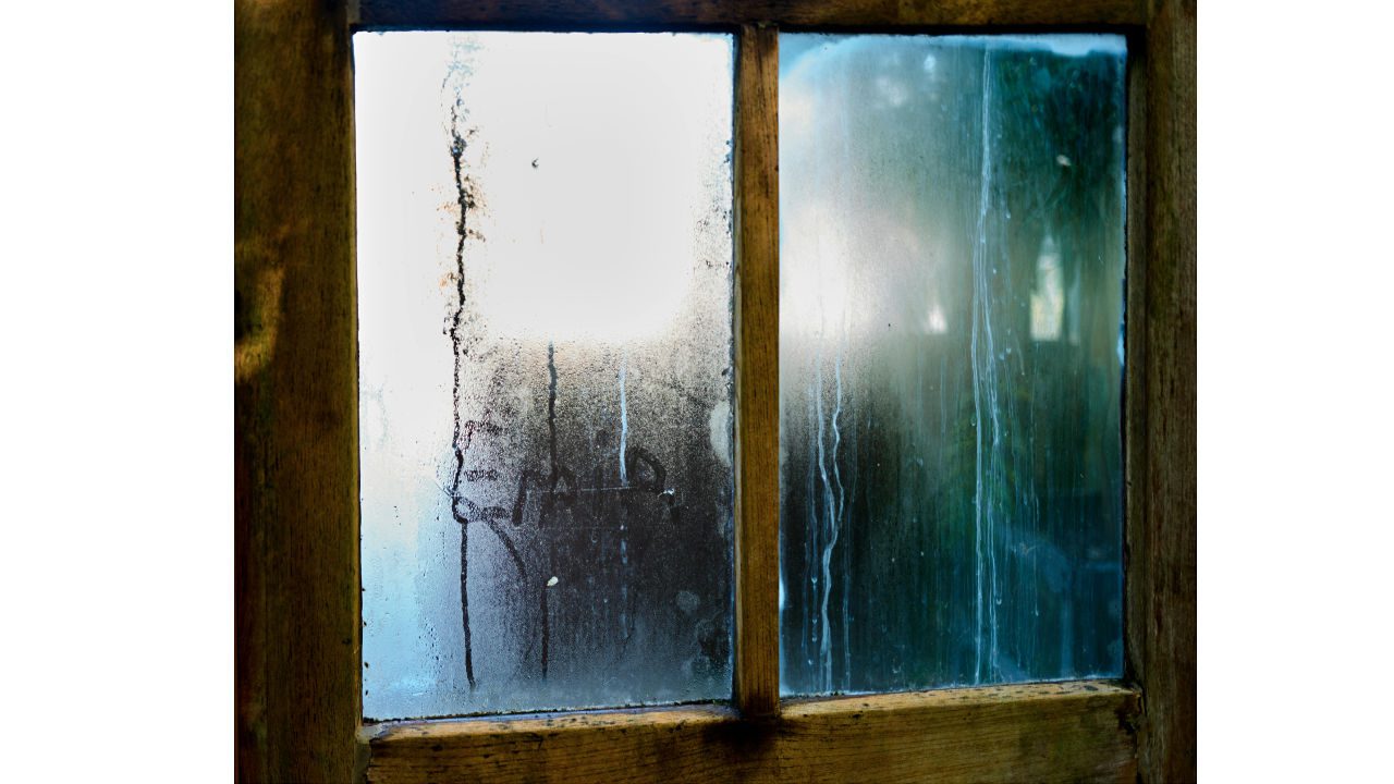 Close-up of old wooden-framed window with foggy, streaked, and dirty glass panes