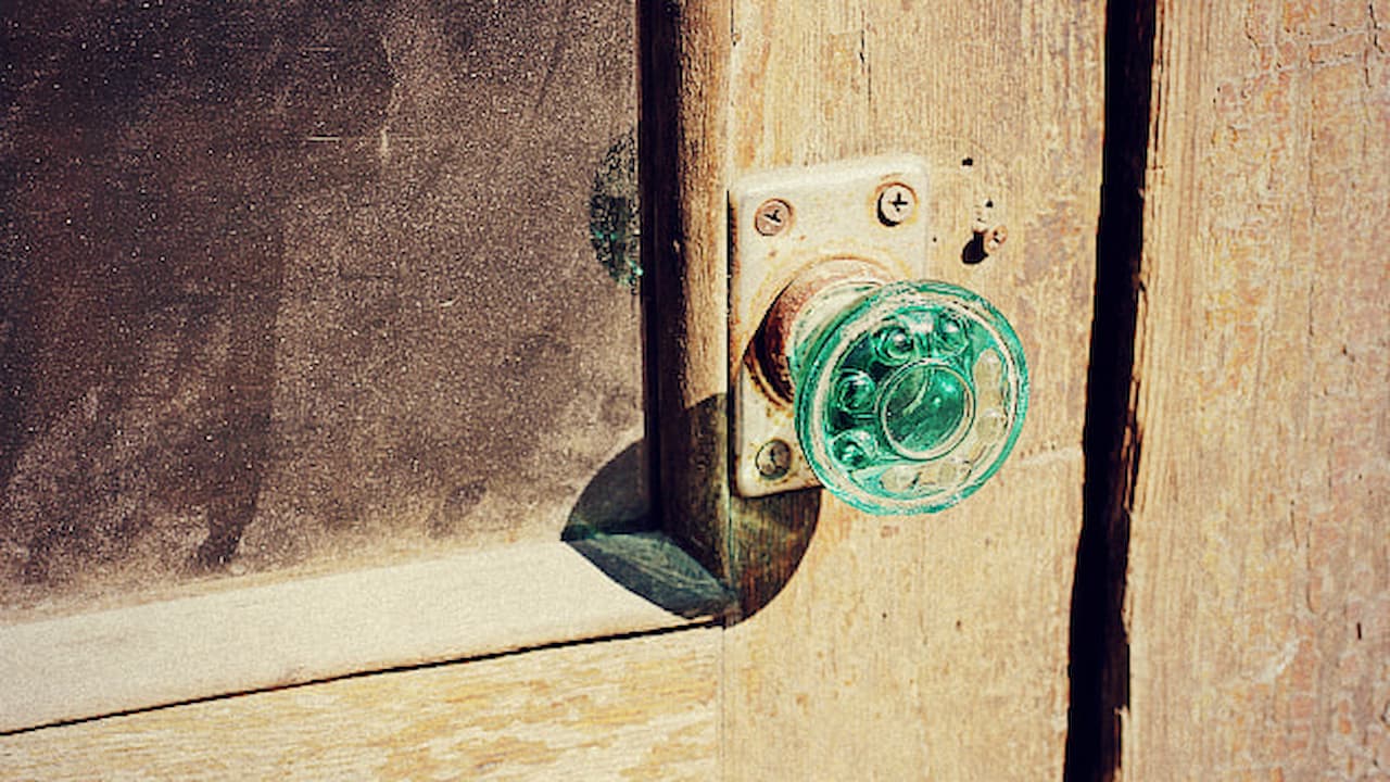Green glass door knob on aged wooden door, vintage hardware style, metal screw plate visible, worn wood surface, sunlight highlighting knob texture