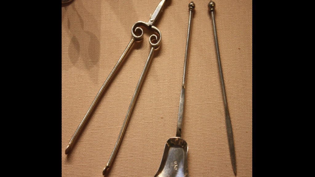 Antique fireplace tools, including pokers, tongs with decorative scroll handles, and a small ash shovel, displayed on beige fabric