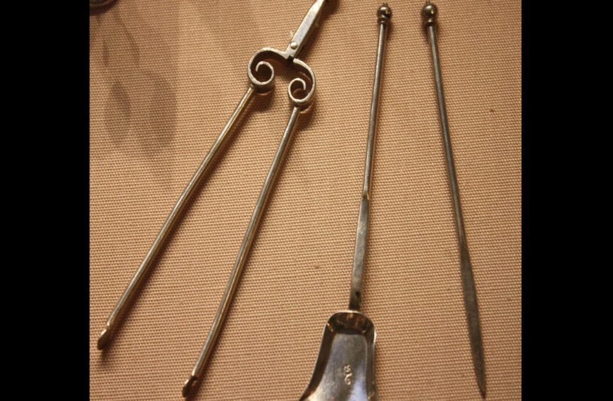 Antique fireplace tools, including pokers, tongs with decorative scroll handles, and a small ash shovel, displayed on beige fabric
