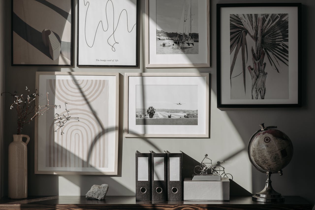 Sunlit wall with a gallery of framed art and photos, globe, binders, and decorative items on a desk