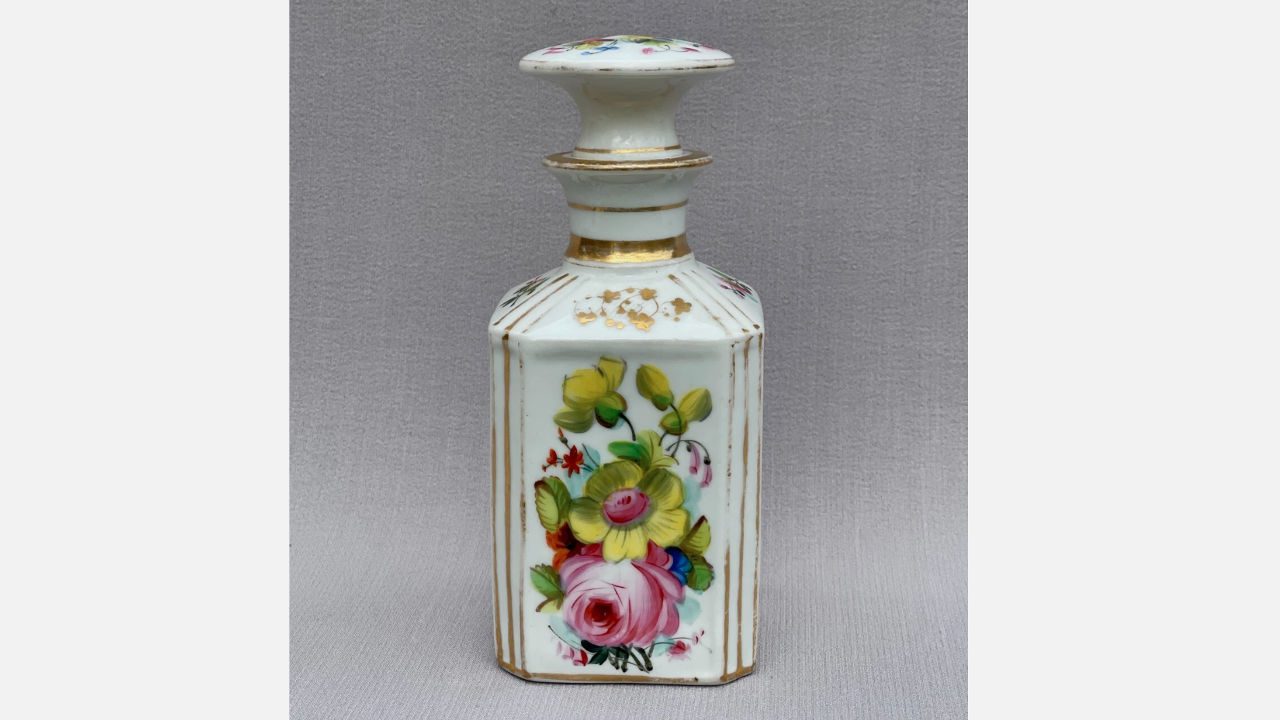 antique French Victorian porcelain jar with hand-painted floral design, gold accents, and round stopper, placed on neutral fabric background