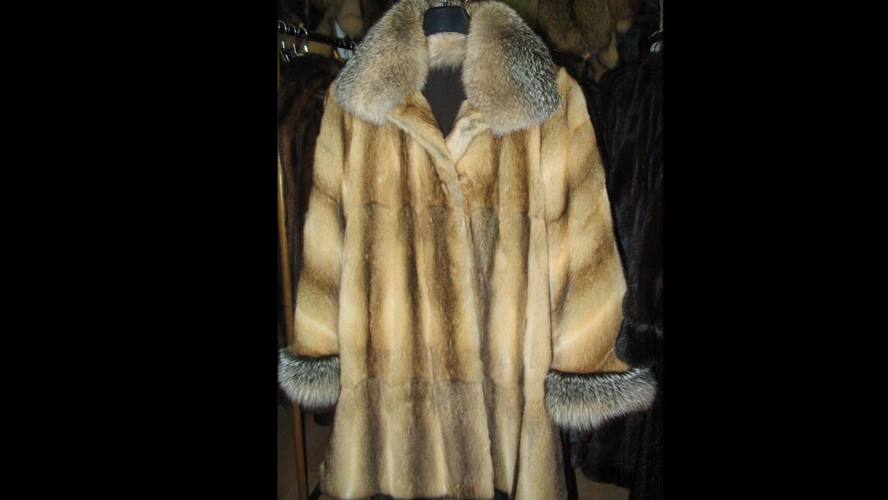 vintage fur coat with light brown body, thick gray fur collar and cuffs, hanging on rack, surrounded by other dark fur coats