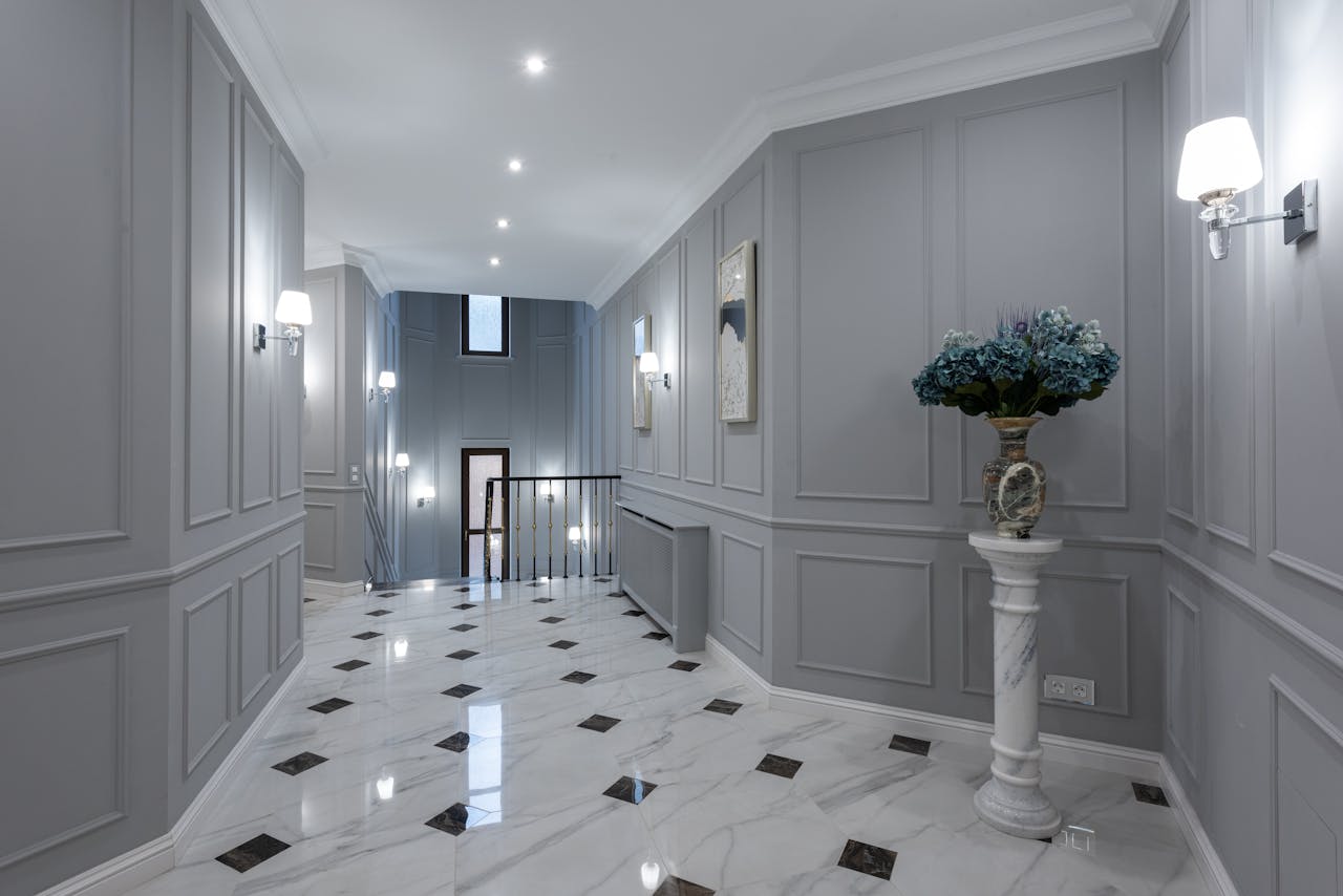 Elegant hallway with gray paneled walls, marble floors, wall sconces, and a decorative pedestal vase