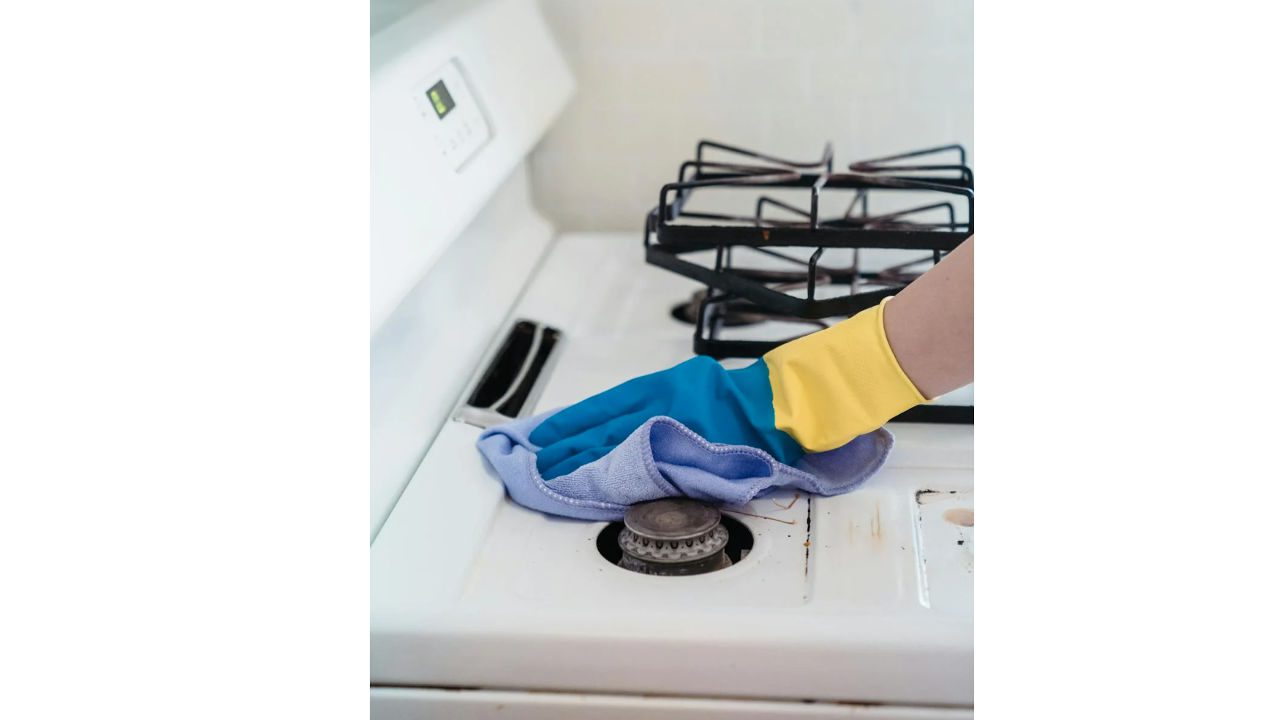 Person wearing gloves cleaning a greasy stove burner with a purple cloth