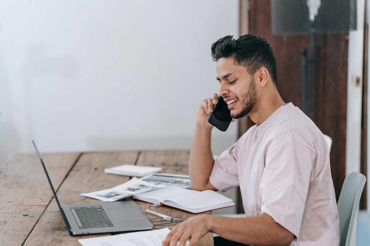 Man sitting at desk talking on phone, laptop and paperwork in front, negotiating or discussing home service
