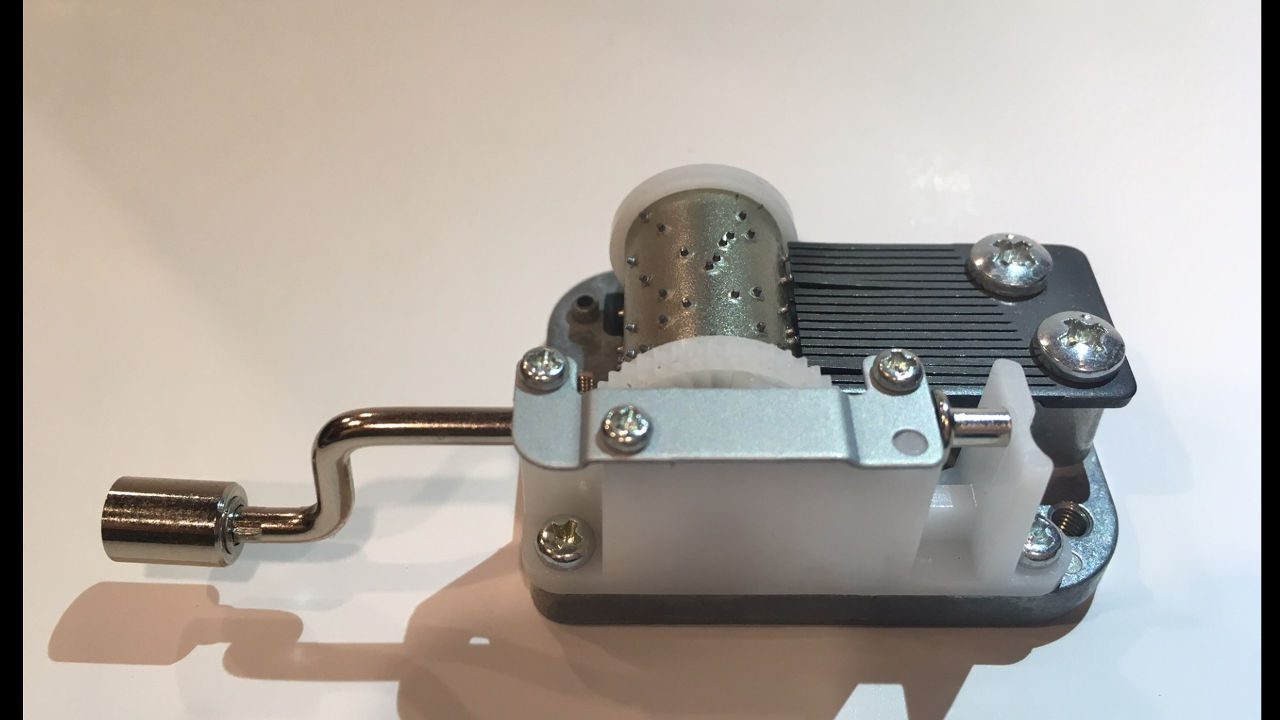 Hand-cranked music box mechanism with exposed metal cylinder and gear components on a white background