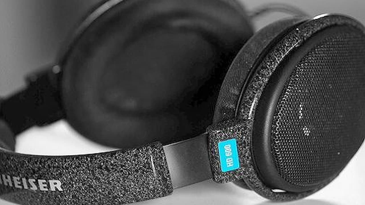 Black over-ear headphones, soft cushioned ear pads, textured headband with branding, blue accent tag on side, studio or indoor lighting, close-up view