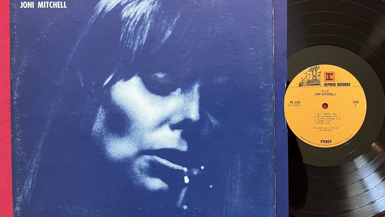 Joni Mitchell – Blue album cover, monochromatic blue tones, close-up of Mitchell’s face in shadow, eyes downcast, minimalist design, emotional and introspective mood