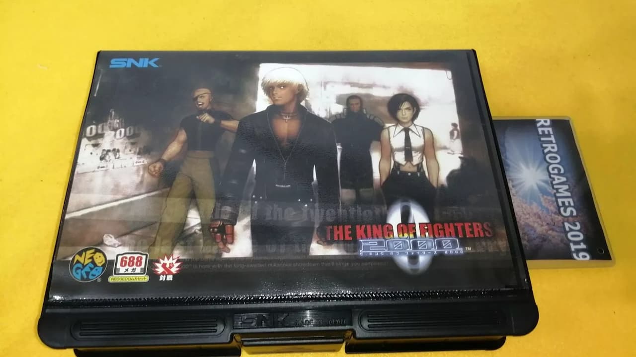 King of Fighters 2000 Neo Geo cartridge, SNK label with character artwork, black plastic casing, Neo Geo logo, retro arcade fighting game
