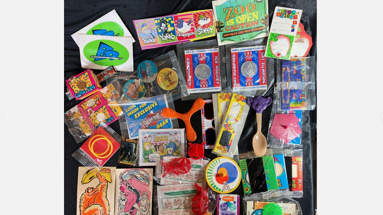 colorful assortment of vintage cereal box toys, stickers, games, puzzles, and premiums from brands like Kraft, displayed on black surface
