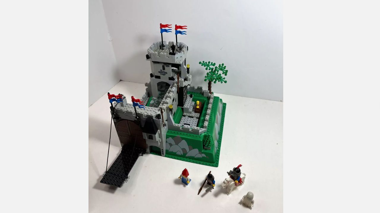 retired LEGO castle set with drawbridge, tower, flags, and four minifigures including knight on horse and ghost, displayed on white surface