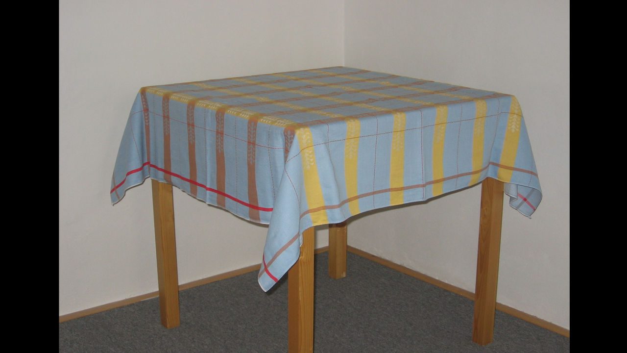 Square wooden table covered with a linen tablecloth featuring vertical yellow, brown, and blue stripes with a red border