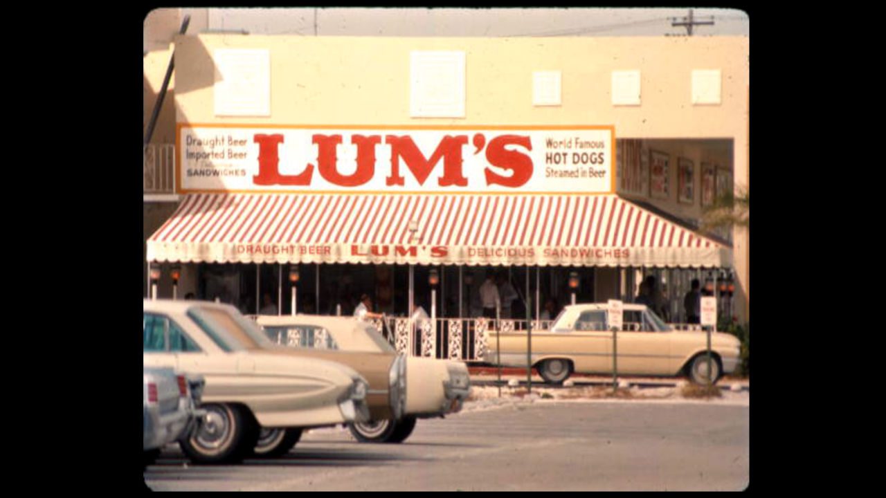 Vintage Lum's restaurant with striped awning, classic cars parked in front, and retro signage