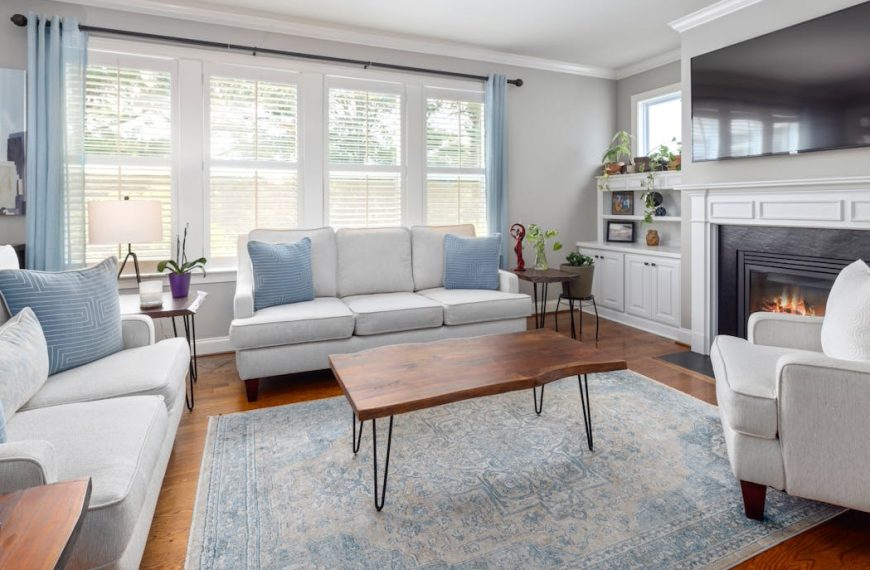 Living room with matching white sofas, blue pillows, wooden coffee table, and a fireplace under a TV