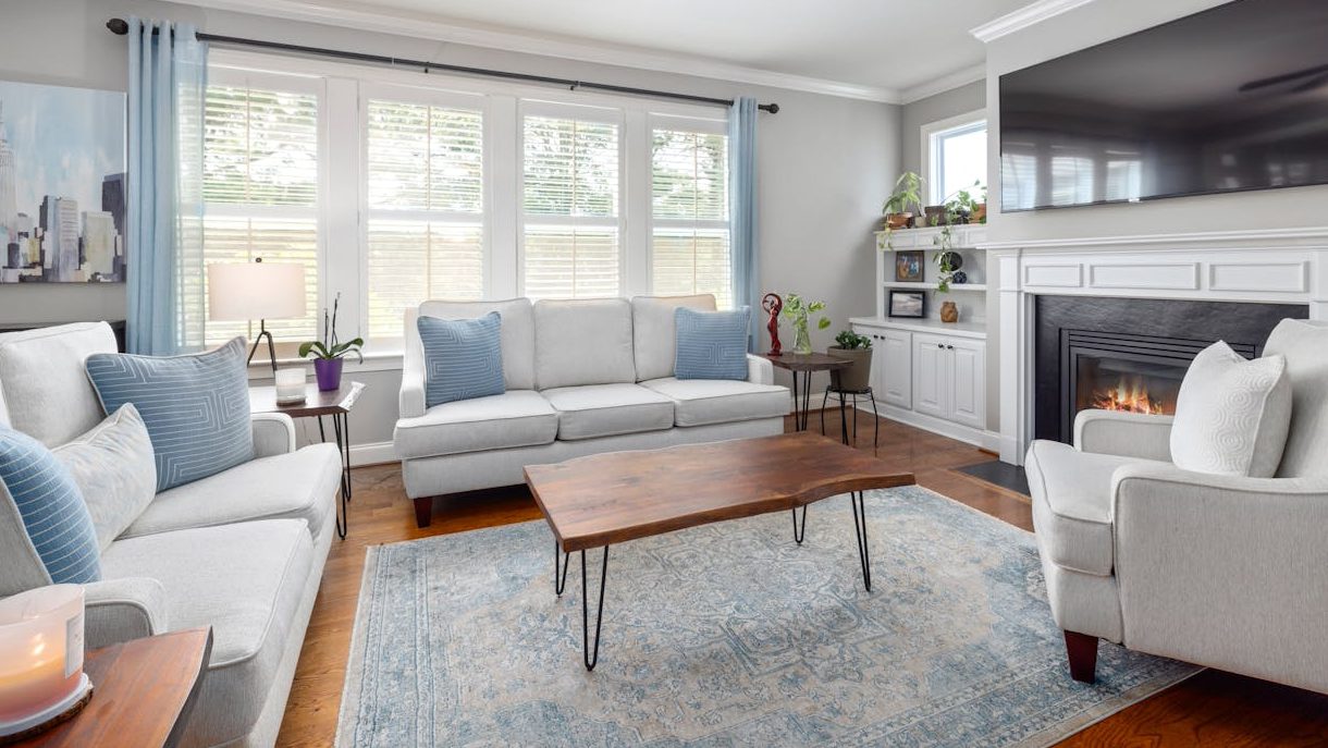 Living room with matching white sofas, blue pillows, wooden coffee table, and a fireplace under a TV