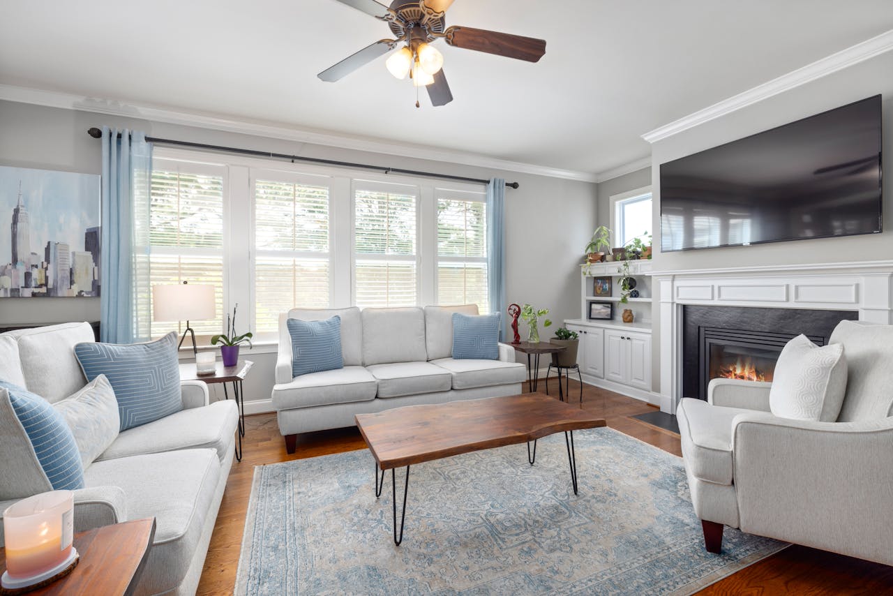 Living room with matching white sofas, blue pillows, wooden coffee table, and a fireplace under a TV