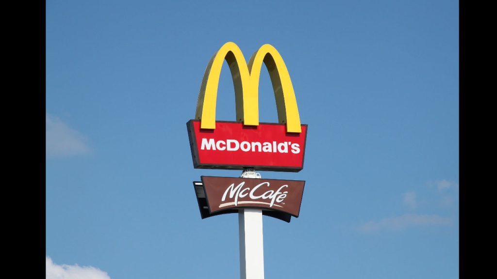 McDonald's sign with yellow arches, red background, white text, McCafé sign below, blue sky background
