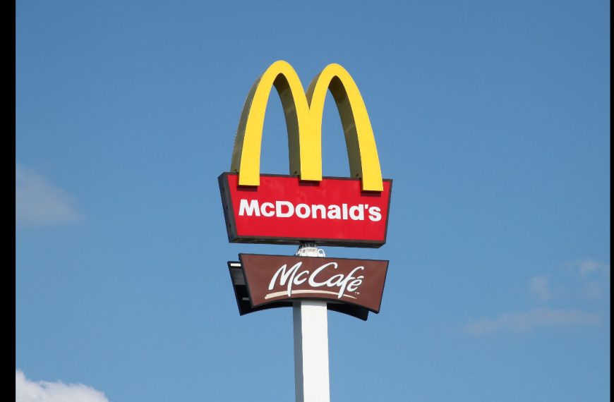 McDonald's sign with yellow arches, red background, white text, McCafé sign below, blue sky background