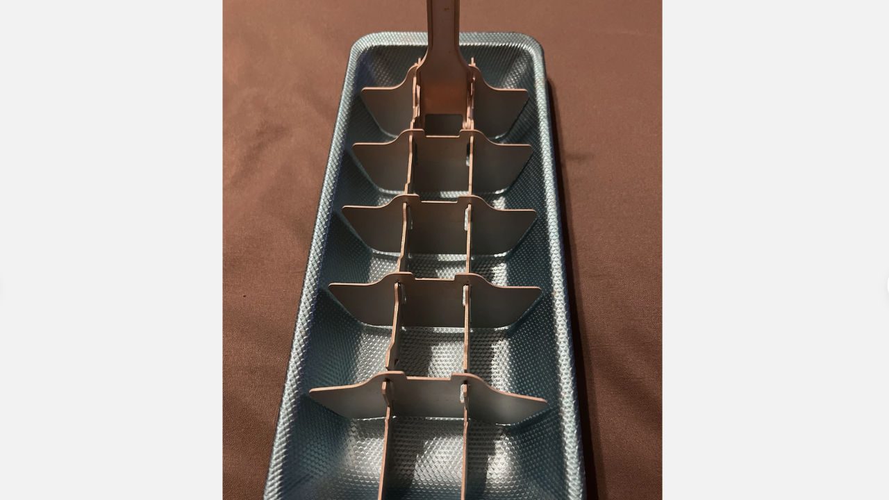 Vintage metal ice cube tray with built-in lever for releasing cubes, placed on a brown surface