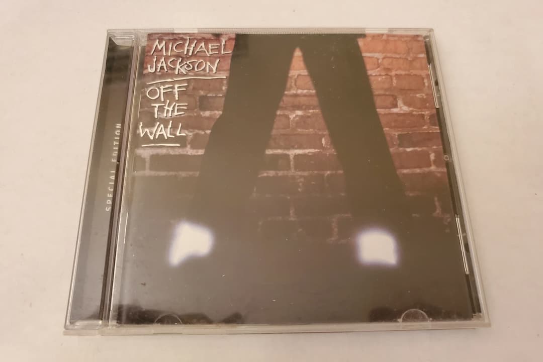 Michael Jackson – Off the Wall album cover, Jackson in a black tuxedo with bow tie, smiling, standing against a brick wall, hands in pockets, warm lighting, youthful and stylish vibe