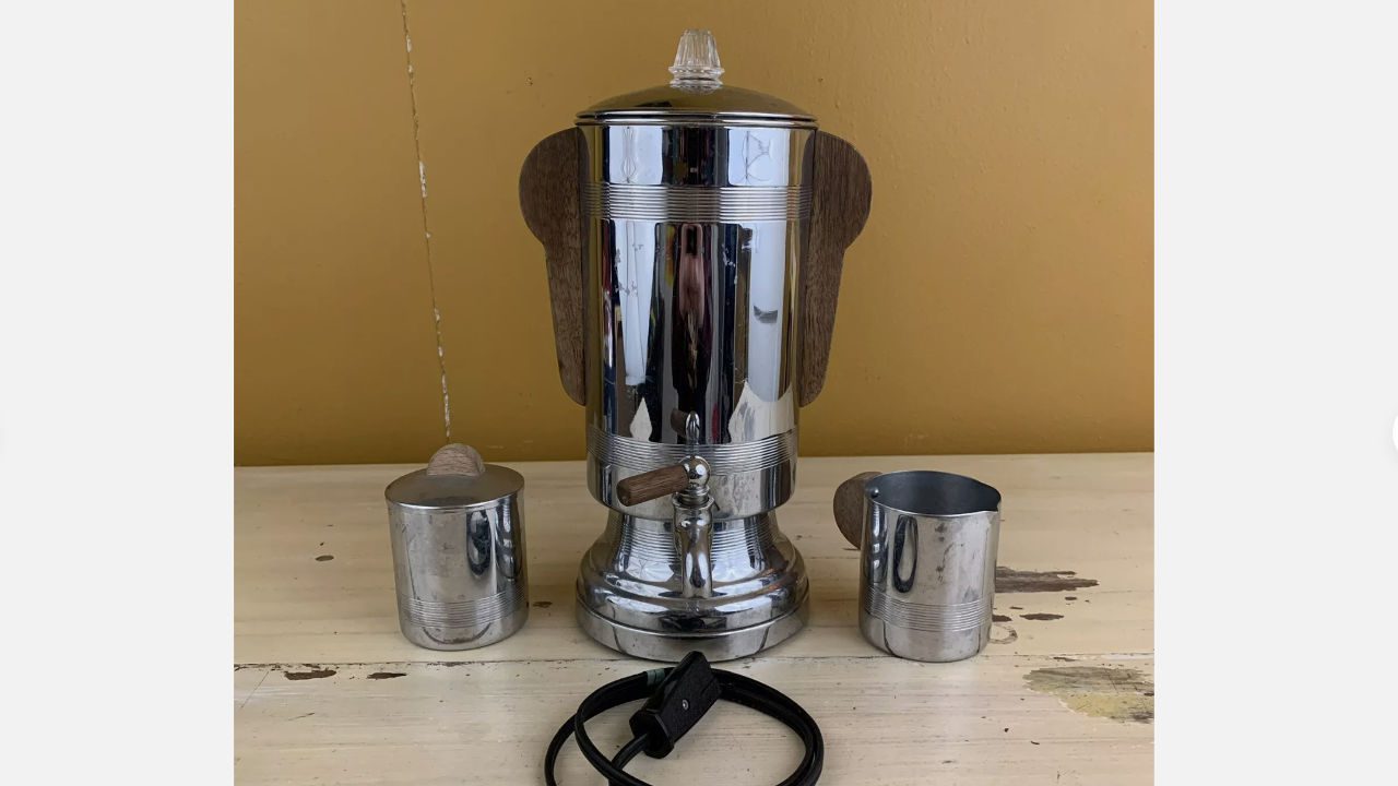 Mid-century chrome electric coffee percolator with wooden handles, two matching cups, and power cord on vintage table