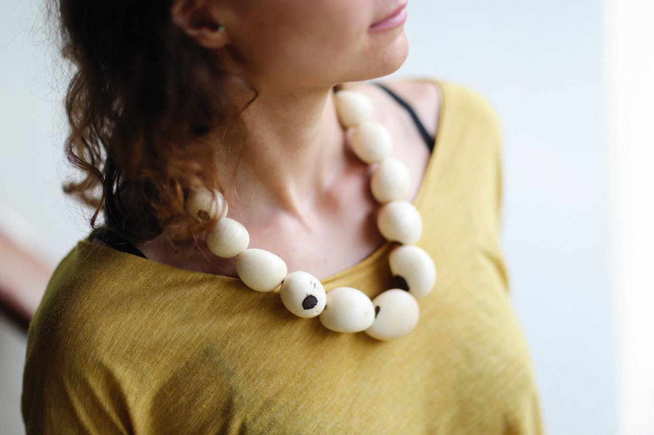 Woman wearing a chunky necklace with large cream-colored beads and a mustard yellow top