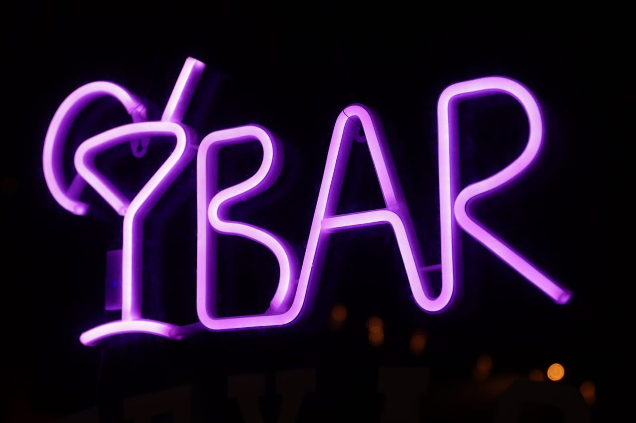 Purple neon sign spelling “BAR” with martini glass design, glowing brightly against a dark background
