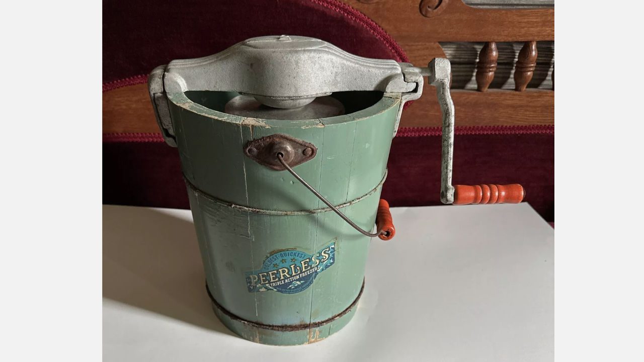 Vintage Peerless hand-crank ice cream maker with green wooden bucket and metal crank handle on table