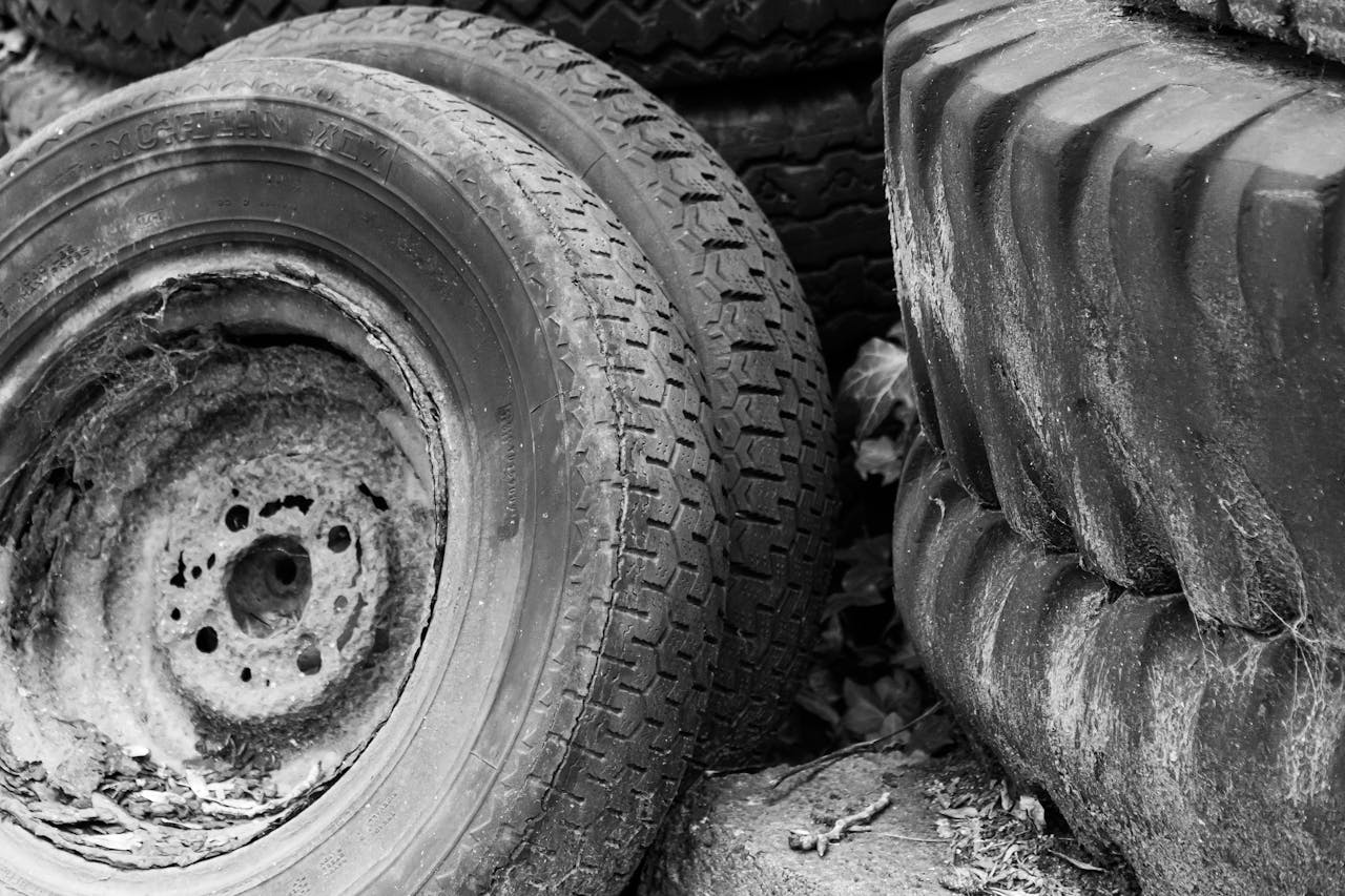 Black and white photo of old, worn-out tires stacked on the ground with visible rust and decay