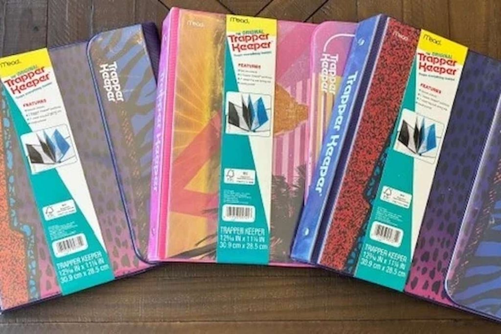 old Trapper Keeper notebooks, colorful covers, Velcro flap closure, worn edges, retro designs, plastic binder rings, stacked on desk