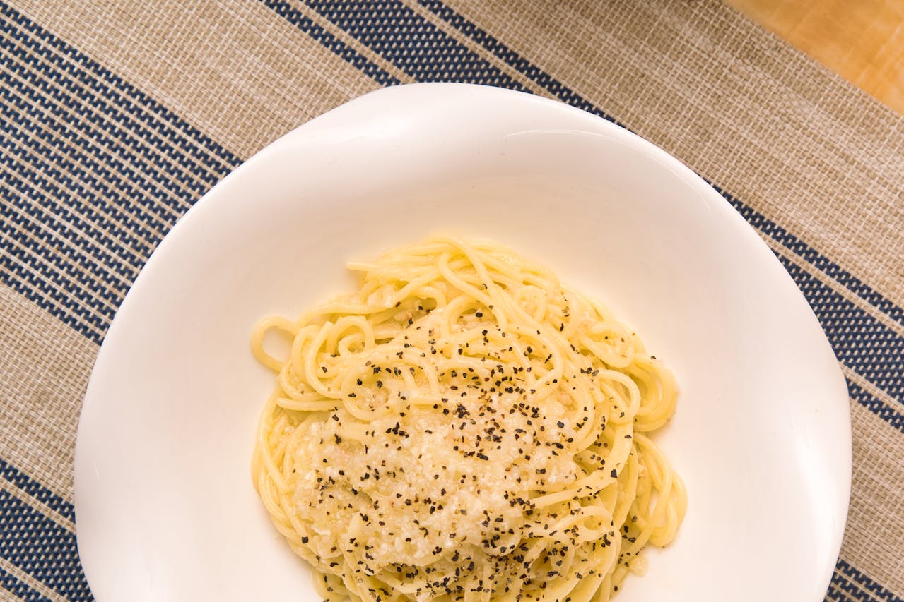 Plate of Cacio e Pepe pasta sprinkled with black pepper and grated cheese in a white bowl