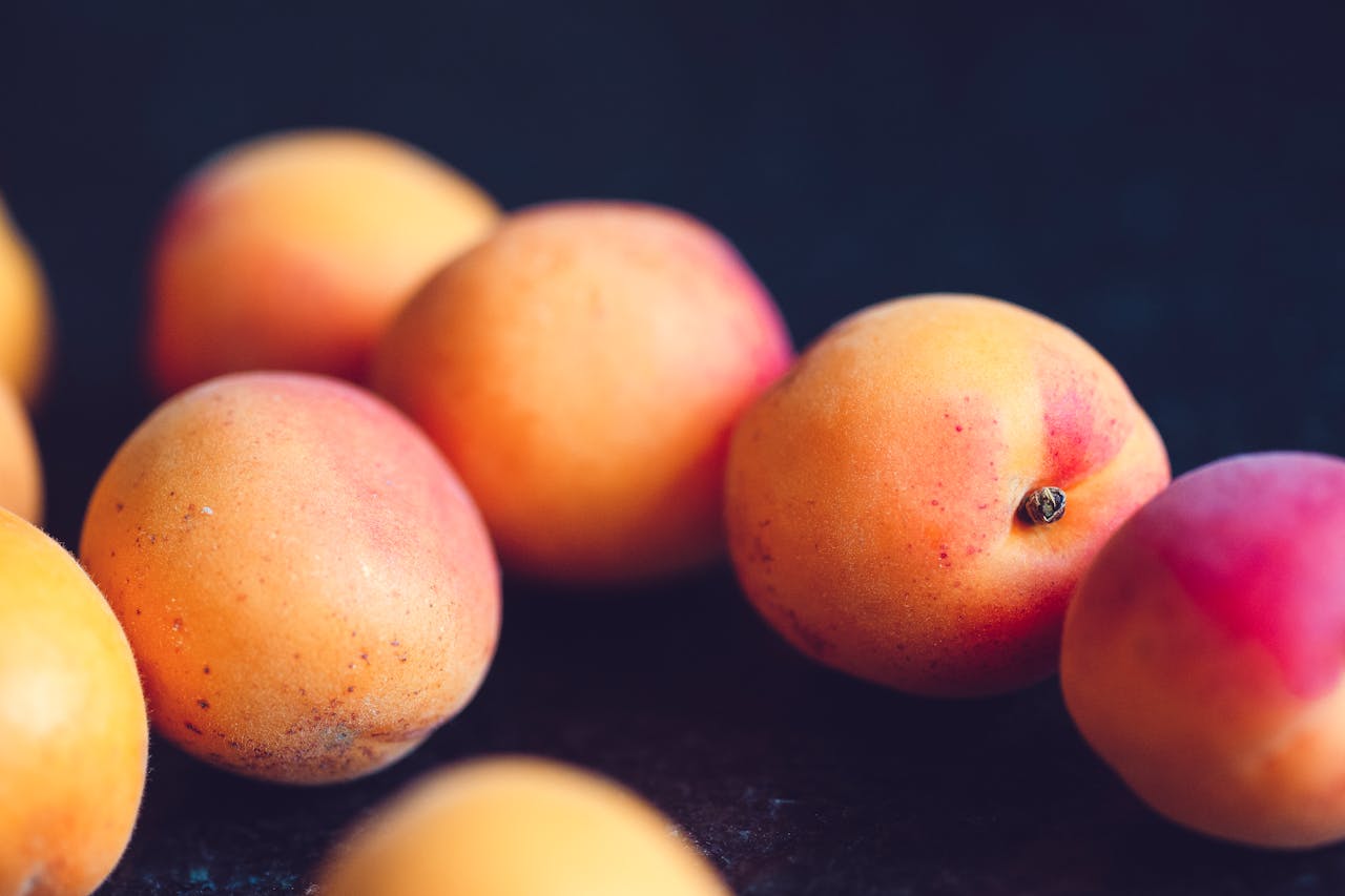 Close-up of ripe peaches with a mix of orange and pinkish-red hues on a dark surface