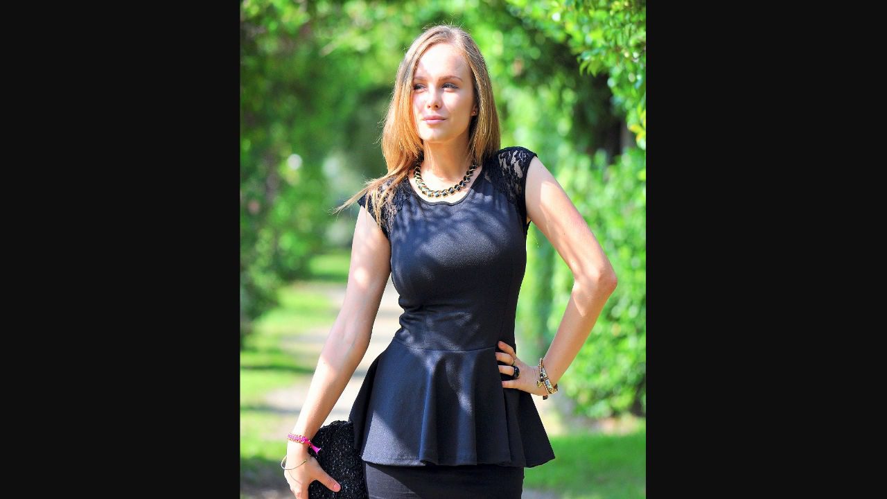 Woman in black peplum top posing confidently in a sunlit garden path
