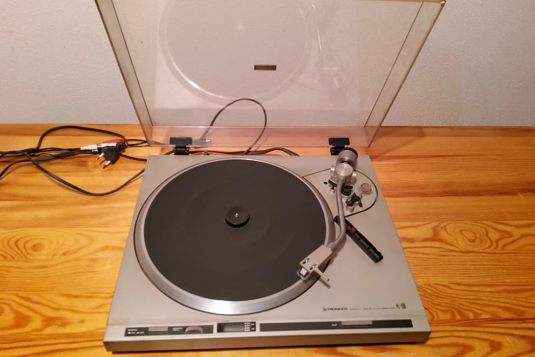 Pioneer turntable, silver and black design, vinyl record spinning, transparent dust cover, tonearm lowered, retro audio equipment, classic hi-fi setup