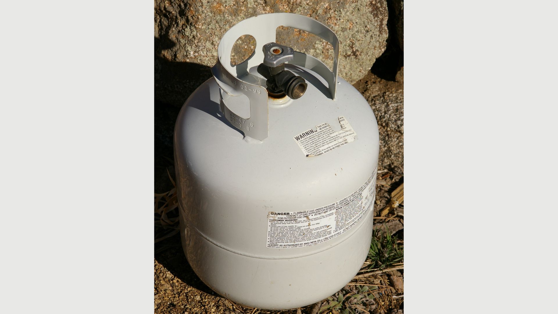A 20 lb (9.1 kg) steel propane cylinder. This cylinder is fitted with an overfill protection device (OPD) valve, as evidenced by the trilobular handwheel. This cylinder has a water capacity specification of 1,318 in3 (21.60 liter, 5.71 U.S. gallons). Propane capacity is is specified as approximately 82% of that (17.8 liter, 4.70 U.S. gallons), to provide space for liquid expansion at higher ambient temperature. The valve assembly is equipped with an automatic pressure relief valve, to allow propane to vent and prevent the cylinder from rupturing.