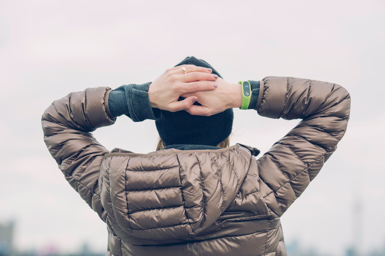 Person wearing a shiny brown puffer jacket with hands resting on the back of their head