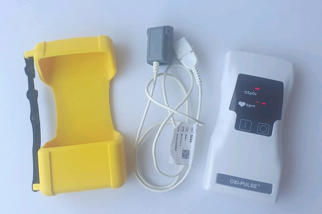 Digital fingertip pulse oximeter, white plastic clip‑on sensor, small LED display showing SpO₂ percentage and pulse rate, rubberized interior pads, compact portable design