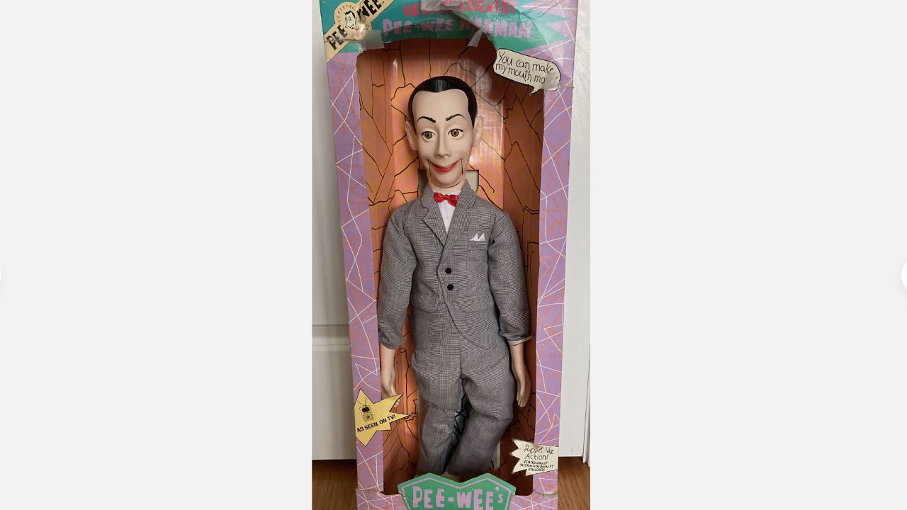 Pee-Wee Herman ventriloquist doll in original box, wearing gray suit with red bow tie, speech bubble on packaging