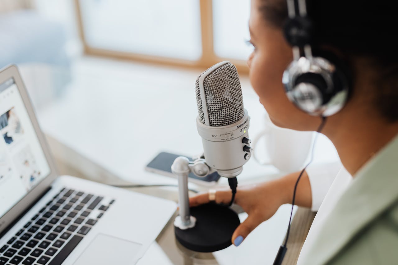 Woman wearing headphones speaking into a professional microphone while recording at a laptop setup