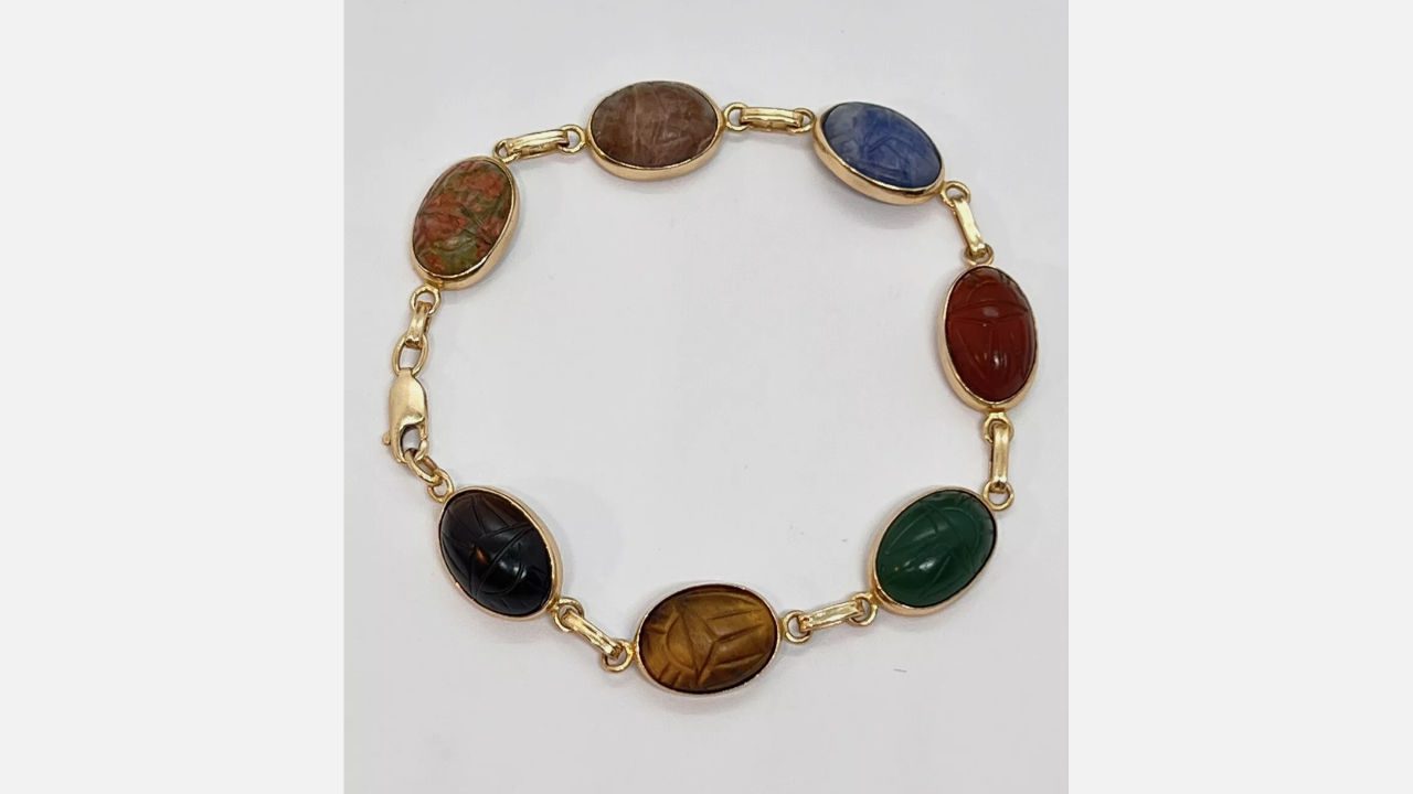 vintage scarab bracelet with gold links, featuring oval carved multicolored stones in red, green, blue, brown, black, and orange tones on white background