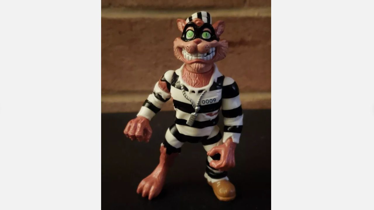 Scratch the Cat action figure in black and white prison stripes, chain necklace, eye mask, standing on dark surface with brick wall background