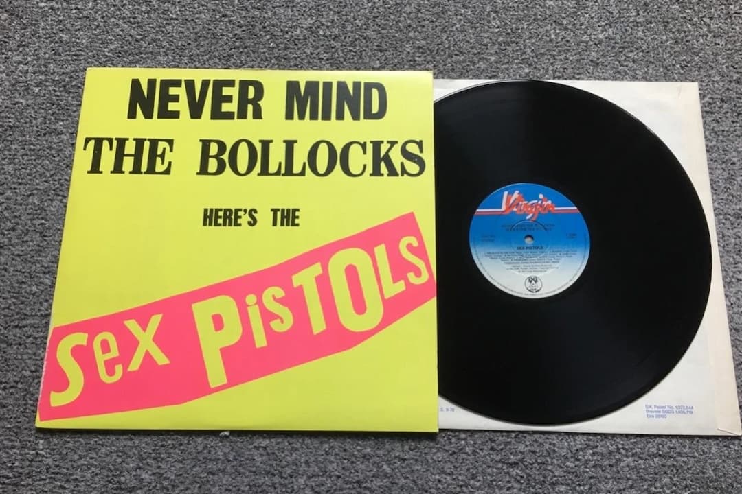 Sex Pistols – Never Mind the Bollocks, Here's the Sex Pistols album cover, bright yellow background, bold black and pink text, ransom-note style lettering, raw and rebellious punk aesthetic
