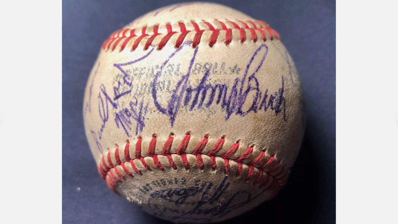 Vintage baseball with multiple autographs in blue ink, visible red stitching, placed on dark blue fabric