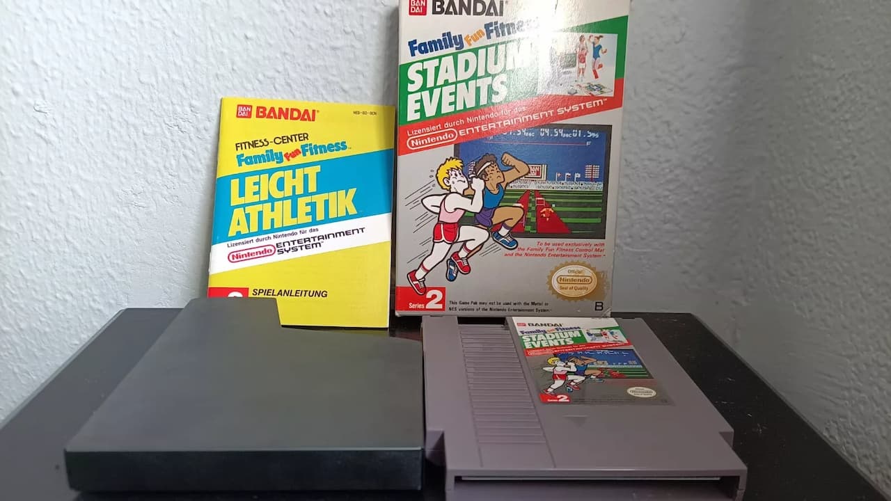 Bandai Stadium Events NES game cartridge, original box, and German instruction manual, placed on a black table against a light gray wall
